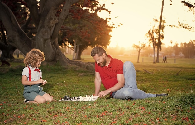 Photo dad and child play logic game father and son playing chess on grass in park fathers day