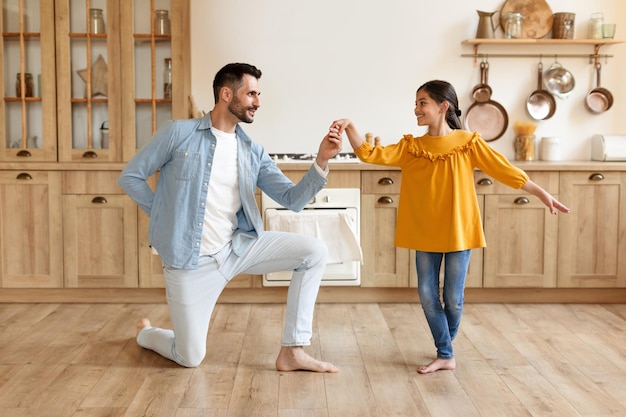 Dad dancing to music with preteen daughter at home kitchen