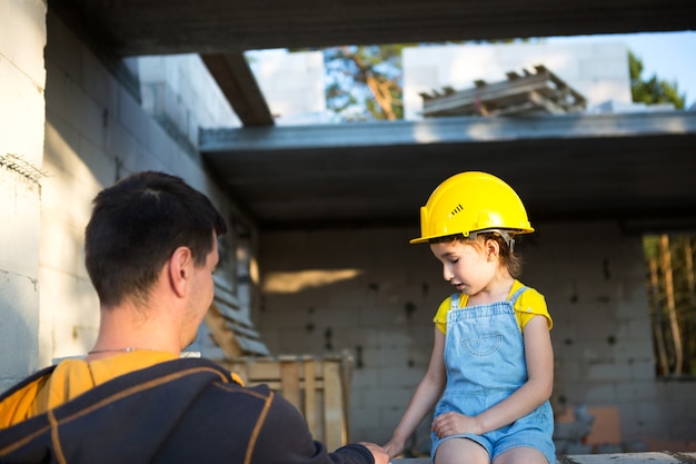 아빠와 딸은 미래의 집 건설 현장에 있습니다. 건축업자의 미래 직업의 선택은 아이에게 상속됩니다. 이사의 기대, 집의 꿈. 모기지, 대출