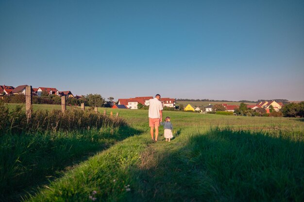 Foto padre e figlia di aspetto caucasico camminano in un prato in un giorno d'estate soleggiato al tramonto un uomo con sua figlia passa il tempo a giocare in natura