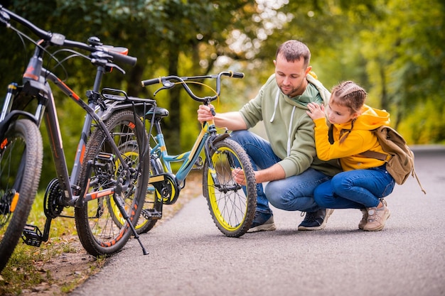 Dad and daughter inspect wheel of children's teenage bicycle on the autumn path of the park