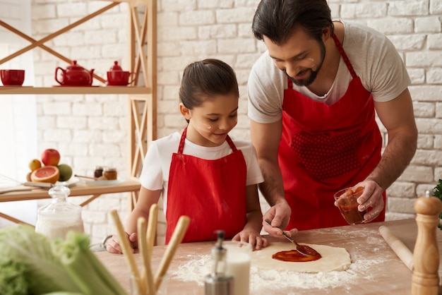 Photo dad and daughter prepare pizza with tomato sauce.