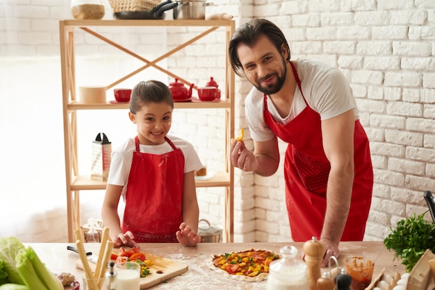 Photo dad and daughter put pepper slices on a pizza.