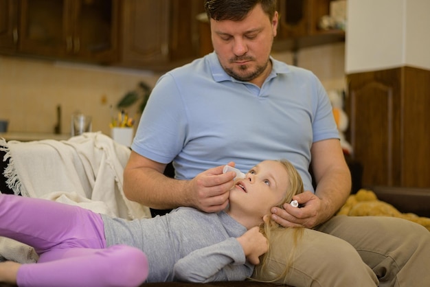 dad drips drops of medicine into the nose of his sick child on the couch at home