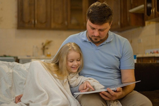 dad entertains the child during illness he looks reads a book a photo book with his daughter home