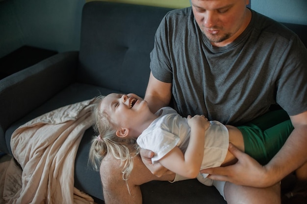 Dad has fun playing with his child at home on the couch tickling him