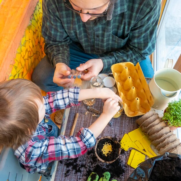 Dad helps his son plant seeds in a peat pot