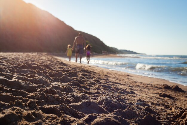 dad and his daughters are walking along the seashore in full focus