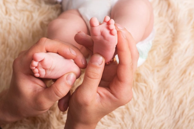 Dad holds in his hands a small baby foots. Small legs of a newborn baby in large hands of dad. Baby foot massage