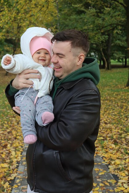 Photo dad holds a little girl in his arms in the park in autumn