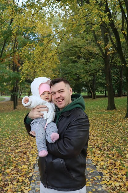 Photo dad holds a little girl in his arms in the park in autumn