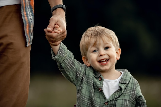 写真 お父さんは幸せな子供の手を握る小さな男の子は微笑む父と子供は一緒に歩いている子供との家族の余暇の休日父の育成父の日フレンドリーな家族の概念
