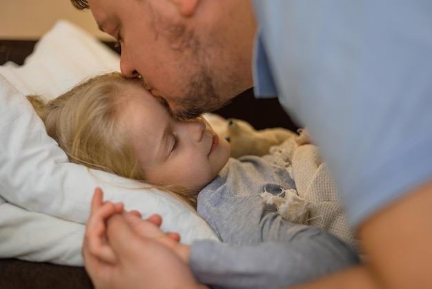 Dad kisses his sick child on the forehead before bed father\
tenderness and care kisses his daughter