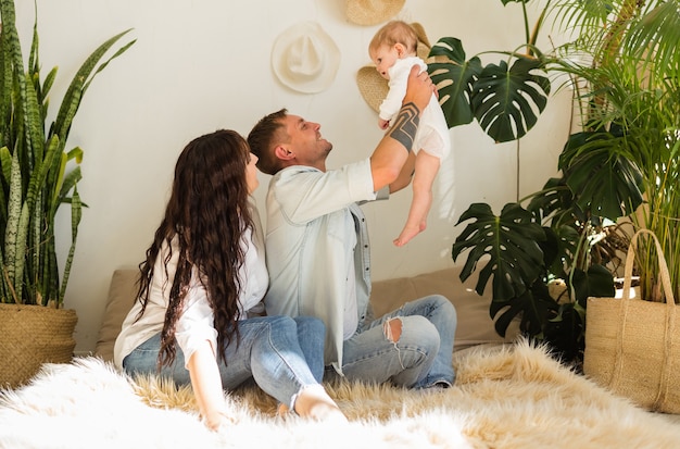 Dad lifts up the baby girl, mom sits on the bed next to him