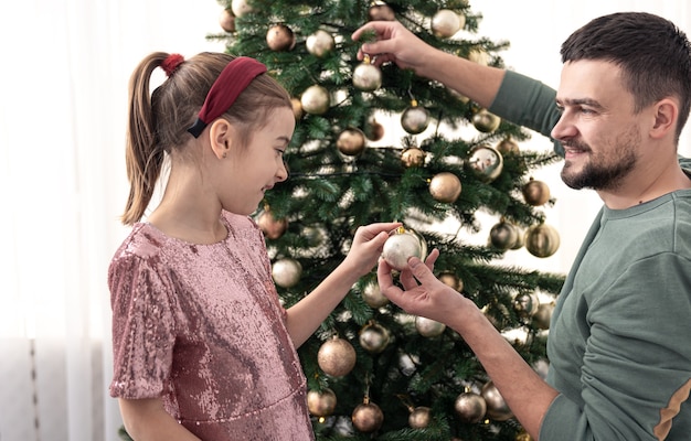 Papà e figlia decorano insieme l'albero di natale, il concetto di preparazione al natale, i valori familiari.