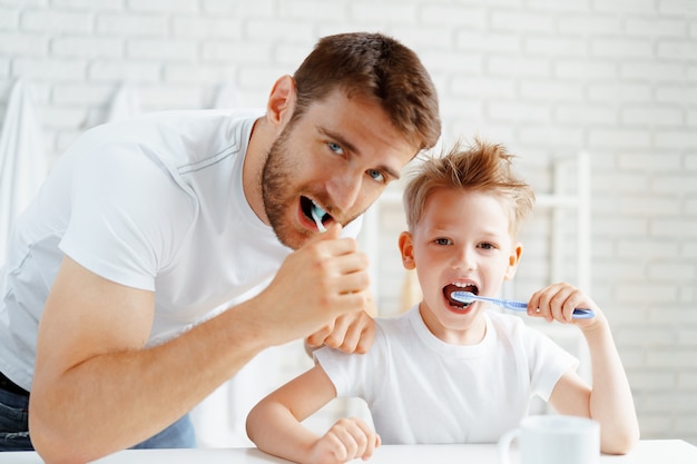 Dad and little son brushing teeth together in bathroom