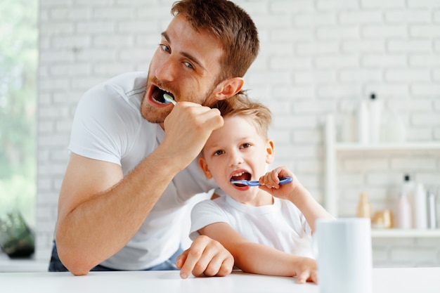 Dad and little son brushing teeth together in bathroom