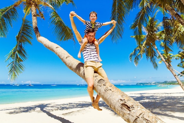 Dad and little son have fun on a coconut tree on a sandy tropical beach. The concept of travel and family holidays.