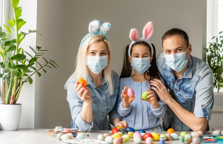 Dad, mom and child daughter at the table in medical masks are painting Easter eggs for the holiday. Happy easter family quarantined coronavirus. Happy at home.