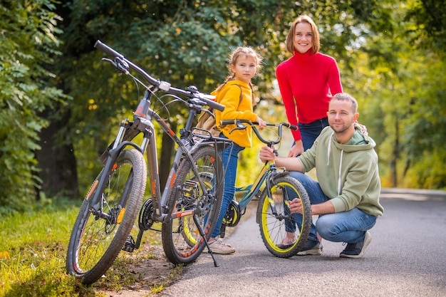 Foto papà, mamma e figlia camminano con le loro biciclette lungo il sentiero autunnale del parco.