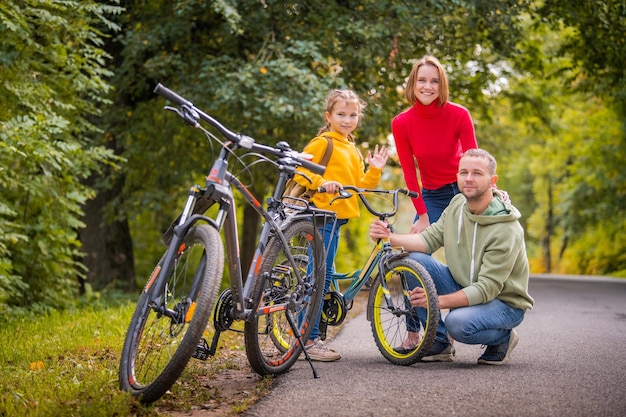 Papà mamma e figlia camminano con le loro biciclette lungo il sentiero autunnale del parco