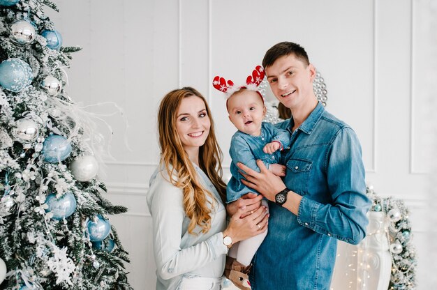 Il papà, la mamma abbraccia la piccola figlia vicino all'albero di natale. buon natale. interno decorato di natale. il concetto di vacanza invernale in famiglia.