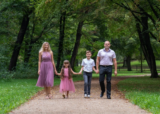 dad and mom son and daughter hold hands and walk along the path in the park