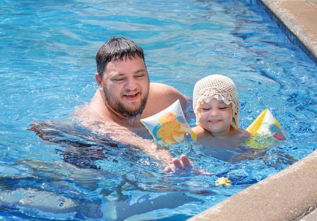 Папа играет со своей дочерью, преследуя игрушку в бассейне.