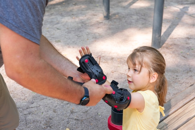 Foto papà indossa gomitiere protettive per la piccola figlia per il pattinaggio a rotelle