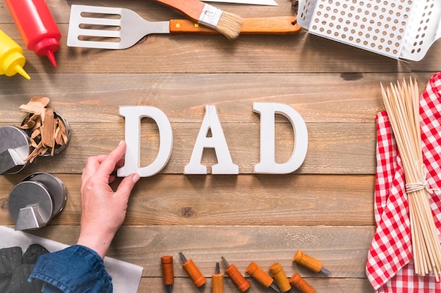 Dad sign for Father's Day with grilling tools on wood background.