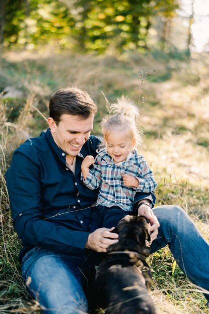 Photo dad sits on the lawn with his little daughter and strokes the dog