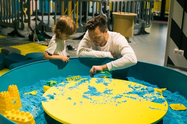 Dad and son are engaged in sand therapy, giving each other joyful emotions. Development of fine motor skills. Relieving stress and tension. Creativity and self-healing.