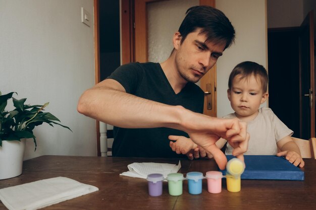 dad and son are painting on canvas at the table with brushes with multicolored paints