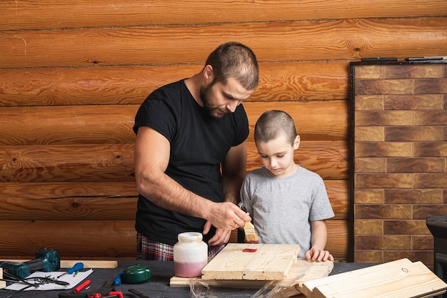 Dad and son are   painting a wooden board with a brush in red