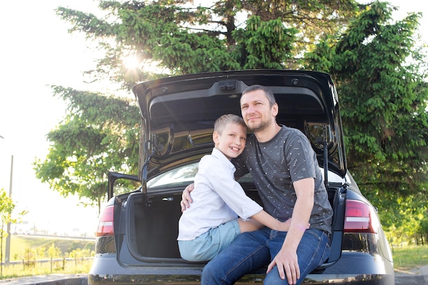 Dad and son are sitting in the trunk of a car at sunset Hugging Dad and laughing