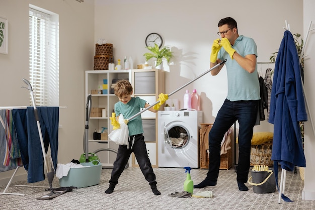 Dad and son dance in the laundry room playing cleaning accessories the little boy holds the mop