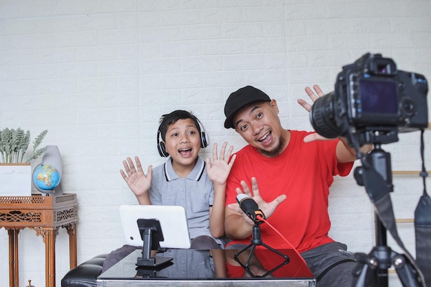 Dad and son greeting online followers while doing video streaming. Asian family spending quality tim