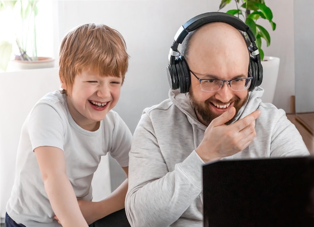 Dad and son laughing having fun, playing video game on laptop at home, spending time together