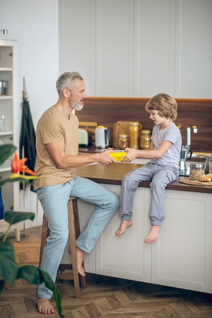 dad and son. mature man in beige tshirt and his son in the kitchen at home