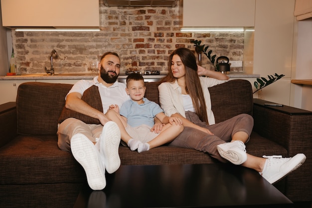 Dad, son, and mom are watching TV on the sofa in the apartment