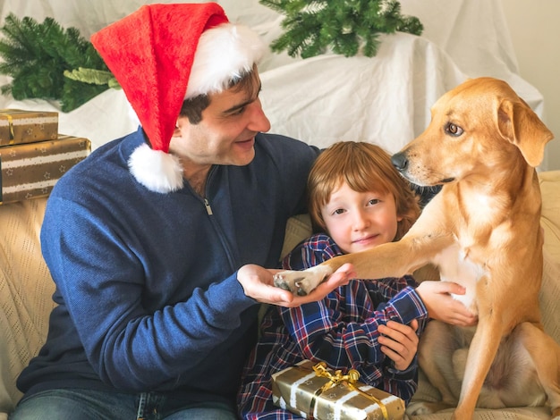 Photo dad and son in santa caps and dog on christmas