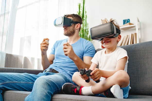 Dad and son sitting on sofa and playing games with VR glasses together