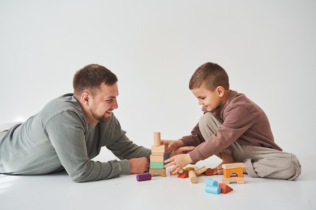 Dad and son smiling having fun and playing colored bricks toy on white background Paternity Caring father with his child