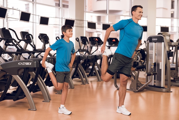 Dad and son stretch their legs in the gym.