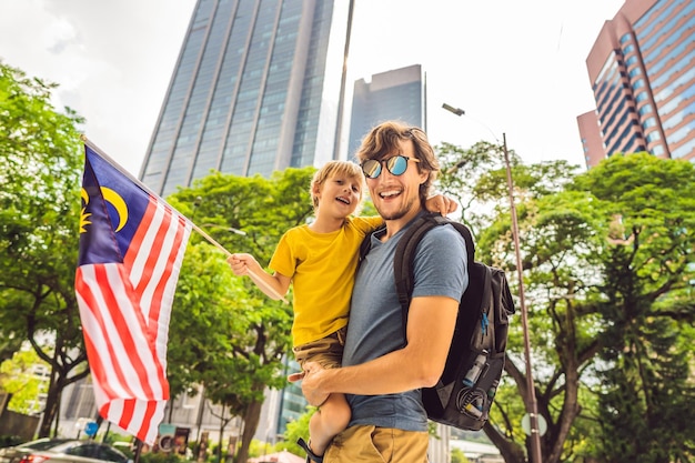 高層ビルの近くにマレーシアの旗を持つマレーシアのお父さんと息子の観光客子供と一緒に旅行のコンセプト