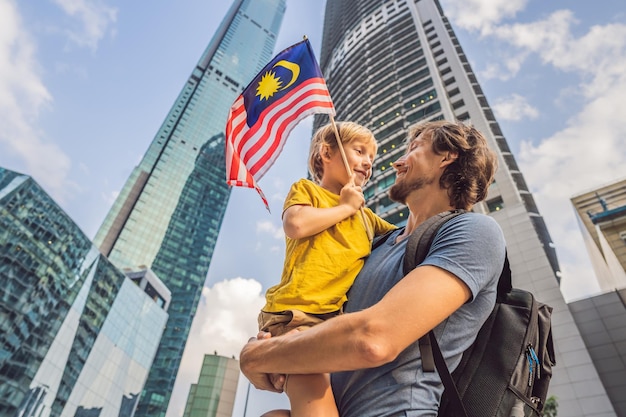 高層ビルの近くにマレーシアの旗を持つマレーシアのお父さんと息子の観光客子供と一緒に旅行のコンセプト