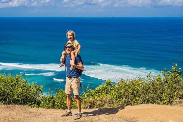 ビーチの上の崖の上でお父さんと息子の旅行者。空の楽園のビーチ、インドネシアのバリ島の青い海の波。スルバンとニャンニャンの場所。キッズコンセプトで旅行。