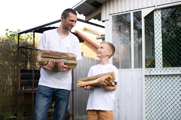 Dad and son in white Tshirts carry firewood and look at each other Place for advertising