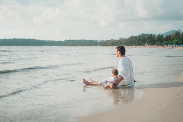 Dad in sunglasses holds the baby in his arms on the beach background.