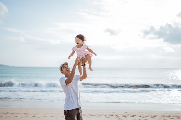 Dad swinging his toddler girl into the air on the beach having fun together